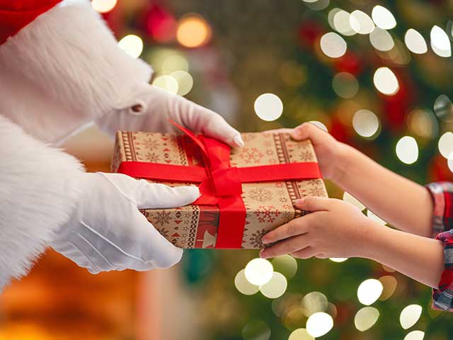 Santa handing a wrapped Christmas gift to a child at Christmas in the Village Pine Mountain Club holiday event